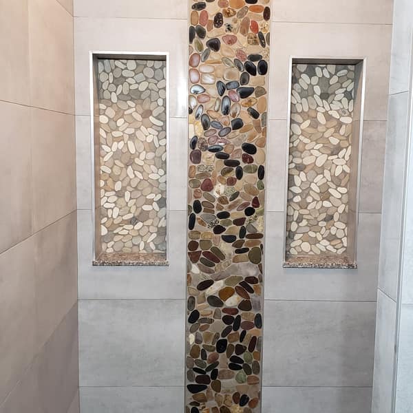Shower wall with a river-pebble accent stripe between two pebble-lined niches