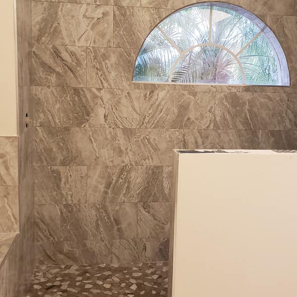 Walk-in shower with stone-look wall tile beneath an arched window