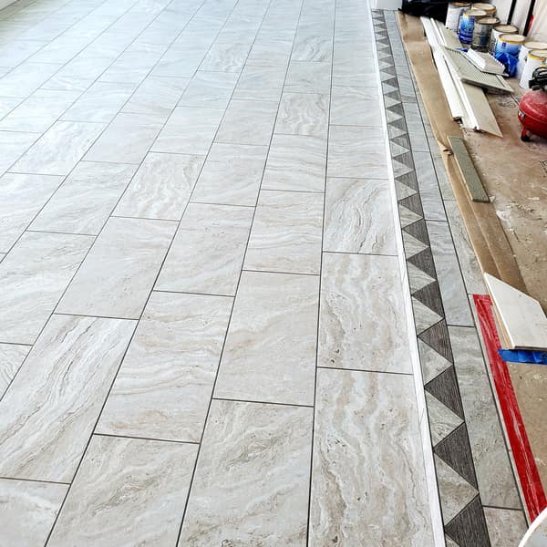 Marble-look tile floor with a decorative mosaic border during installation