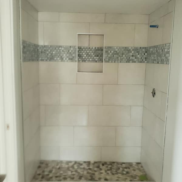 Shower with white wall tile, a mosaic accent band, a niche and a pebble floor