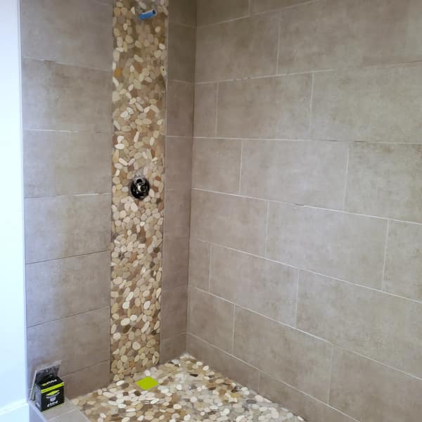 Shower with beige wall tile, a pebble accent stripe and a pebble floor