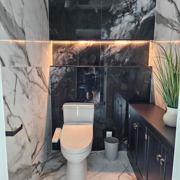 Water closet with white and black marble-look porcelain tile and a lit recessed shelf