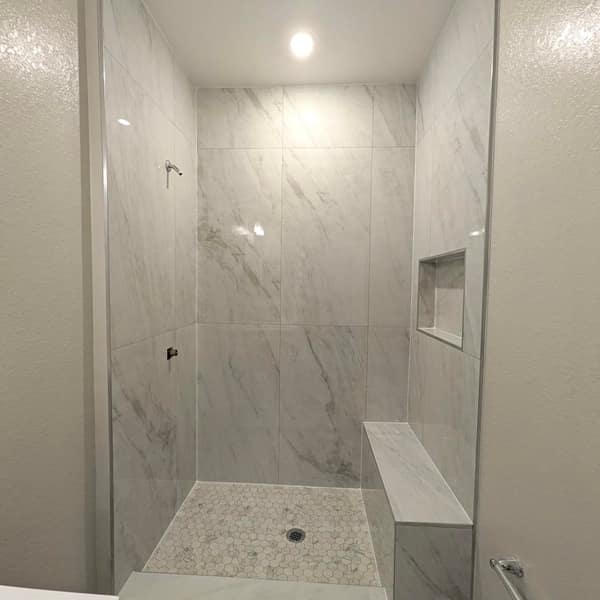 Walk-in shower with large white marble-look wall tile, a bench, a niche and a hexagon mosaic floor