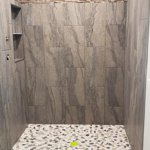 Walk-in shower with large gray tile walls, a niche and a pebble floor